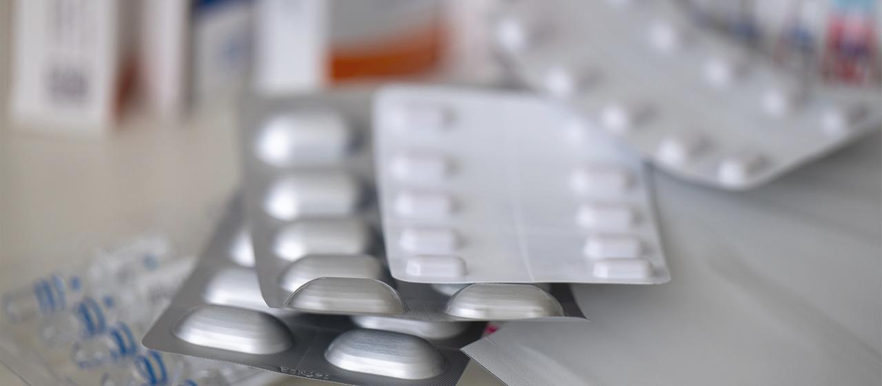 Mehrere Packungen mit Tabletten, Pflastern und Tropfen liegen auf einem Tisch.